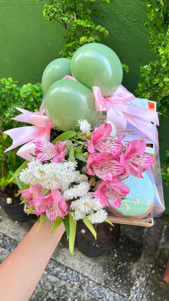 Cesta personalizada com balões verdes, flores e itens de presente.
